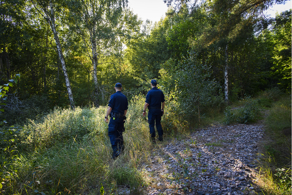 Bilden visar två uniformerade poliser som befinner sig ute i skogen.