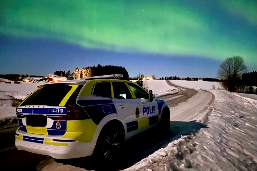 Polisbil körandes på vinterväg med norrsken