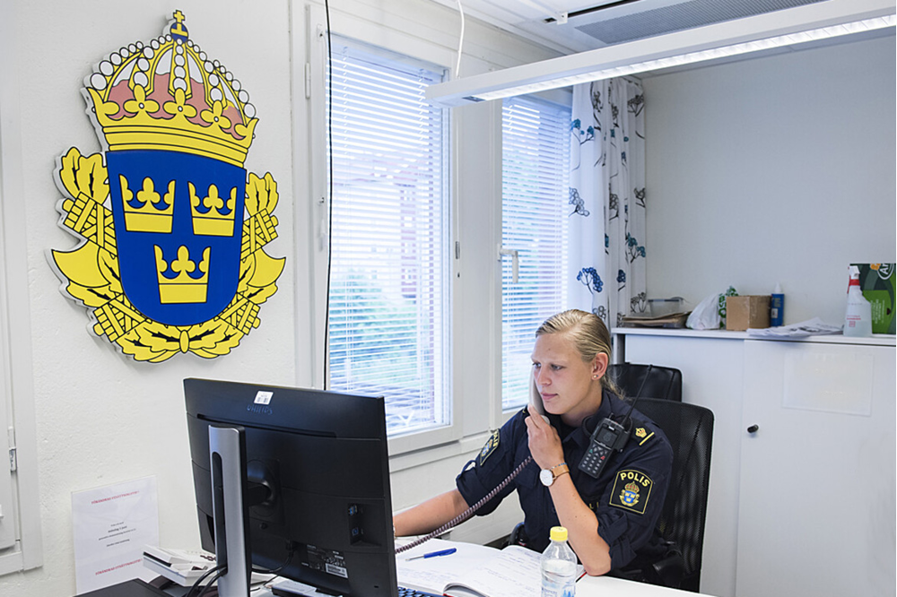 Kvinnlig polis i telefon bakom ett skrivbord.