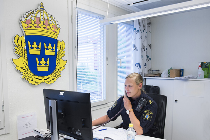 Kvinnlig polis i telefon bakom ett skrivbord.