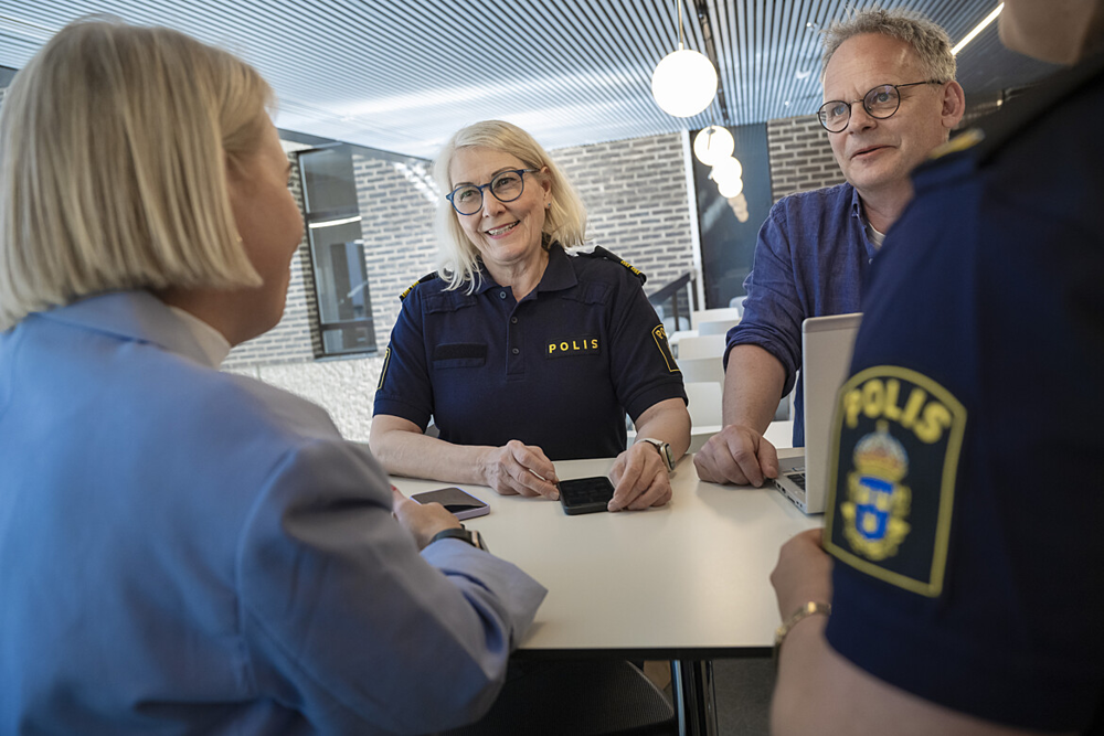 Två personer som ler mot kameran och två med ryggen emot. Den ena som ler har poliskläder på sig