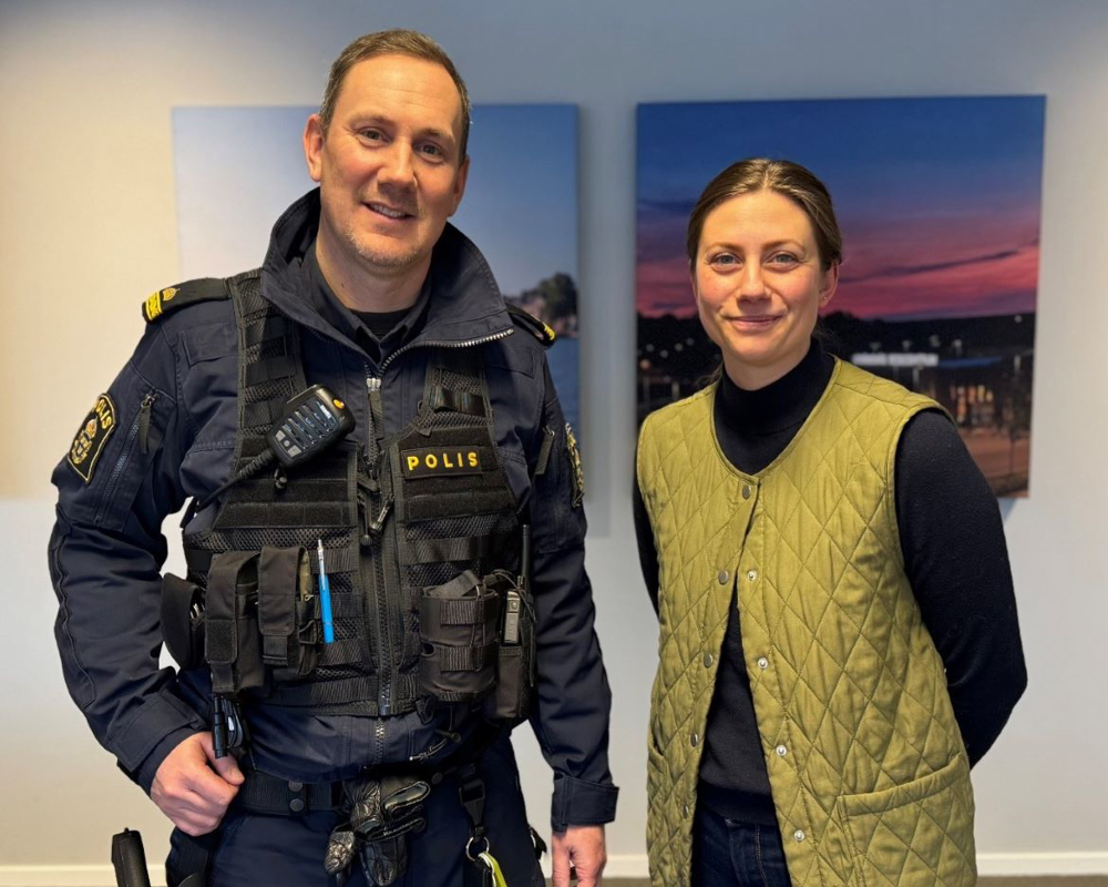 En man i polisuniform står bredvid en civil kvinna. De ser glada ut.