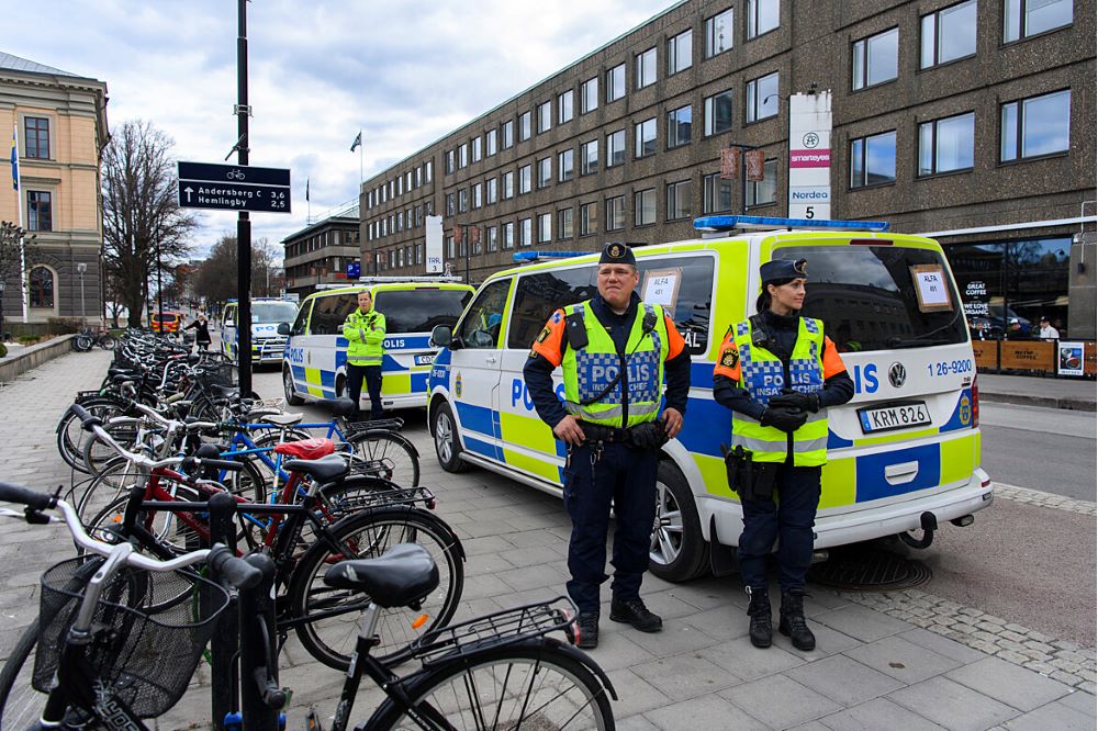 Två polisklädda personer står intill  polisbuss som är parkerad. i bakgrunden syns gata och husvägg  och framför poliserna flera cyklar som är i ett cykelställ