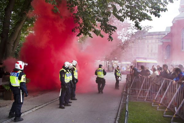 Poliser står framför en folkmassa vid en demonstration, omgivna av röd rök. Foto.