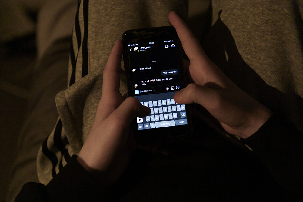 Mörkt rum, person med mobiltelefon i knät, skriver på telefonen