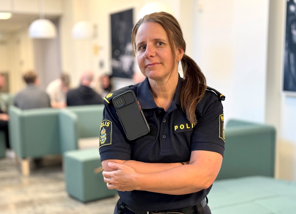 Polis står inomhus. Hon har armarna i kors och tittar in i kameran. 