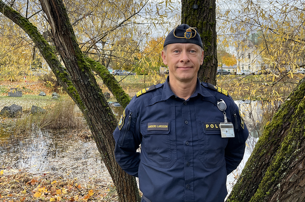 En man i polisuniform står utomhus vid ett träd.
