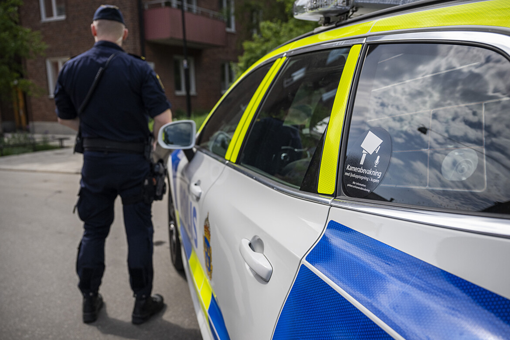 Polis med bakåtvänd rygg står bredvid polisbil i stadsområde