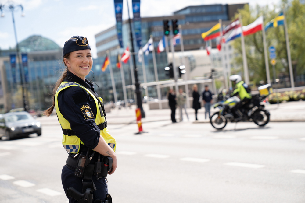 Poliskvinna står intill en väg och ler mot kameran. 