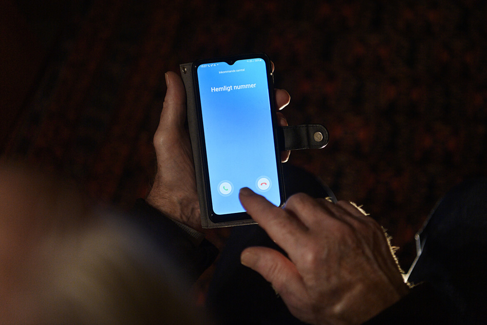 En äldre man håller i en mobiltelefon. 