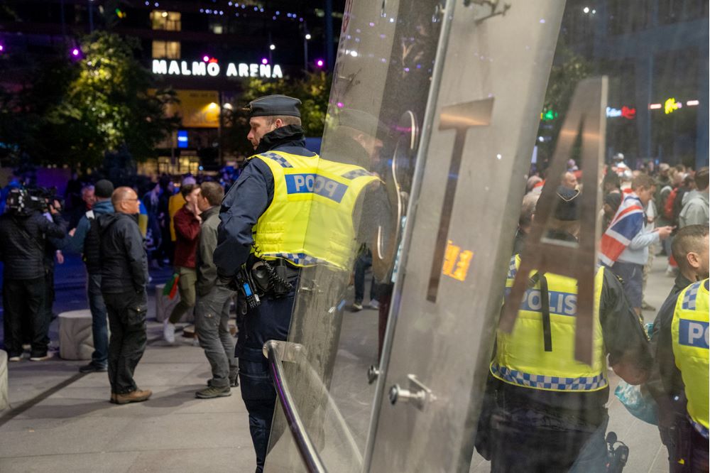 Bild tagen på kvällen. En manlig polis står halvt bortvänd från kameran. I bakgrunden syns e folkmassa och en neonskylt med texten Malmö Arena.