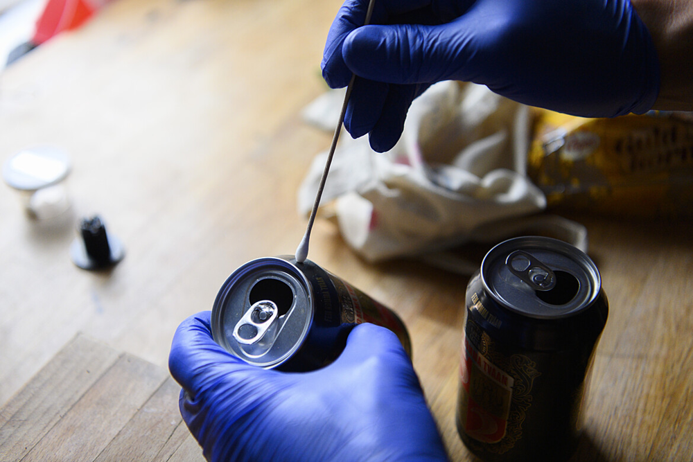 En forensiker drar med en tops på en aluminiumburk för att fånga dna-prov från salivresterna. 