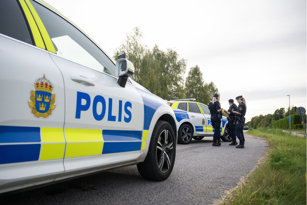 Tre poliser står vid en polisbil och ytterligare en polisbil syns i förgrunden. Foto.