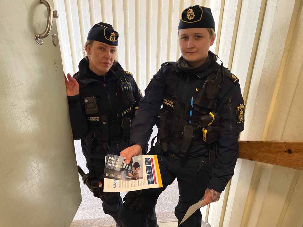 Två kvinnliga poliser står vid en dörr. De lämnar fram informations material.