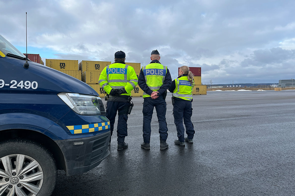 Bild utomhus i hamn. Ryggarna på tre poliser syns och i förgrunden en del av en bil.