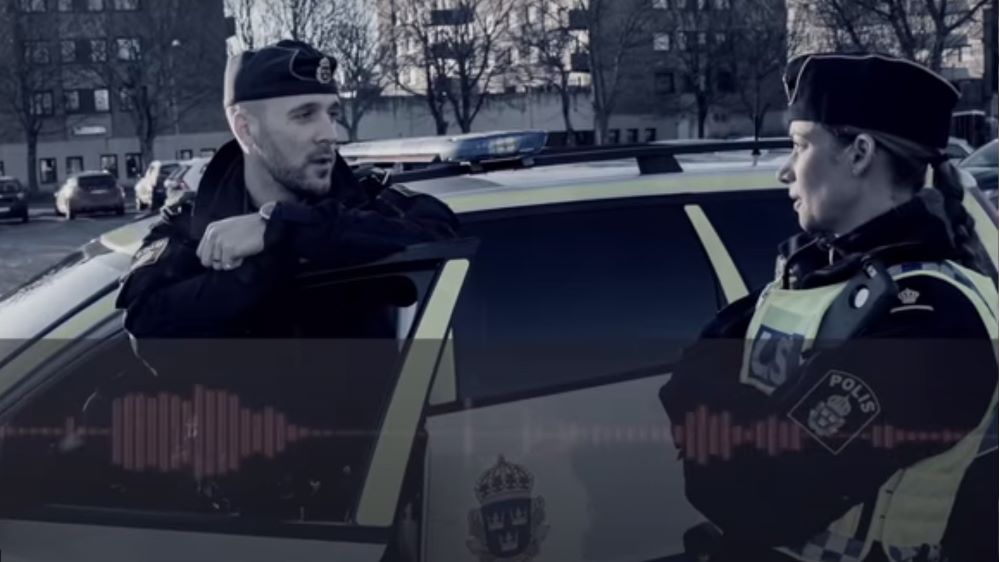 Skärmdump från filmen. Två poliser står vid en polisbil. Frekvensmarkering från bedragarens röst ligger ovanpå bilden.