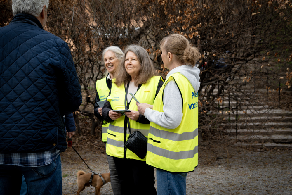 Foto på tre volontärer som står och samtalar med medborgare. I handen har de broschyrer med information om brott i nära relation.