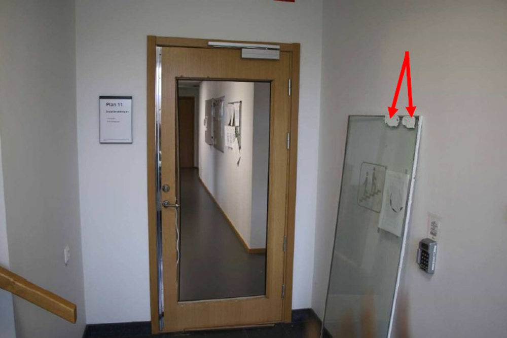 Dörr i trapphus, på sidan, lutande mot väggen står glaspartiet från dörren som har tagits ut.