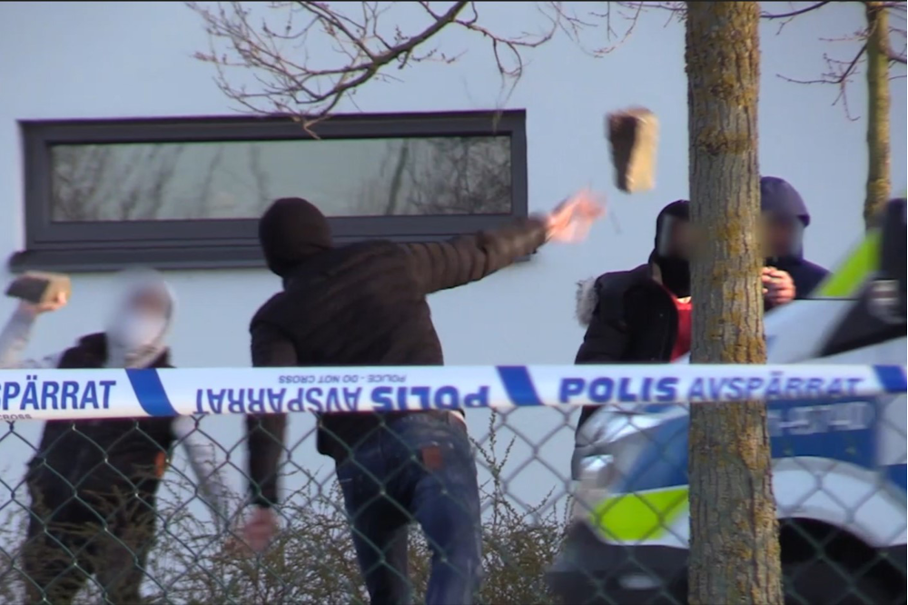 Bild på person som kastar en gatsten mot ett hus