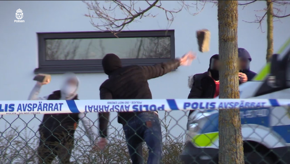 en man kastar en stor gatsten mot personer