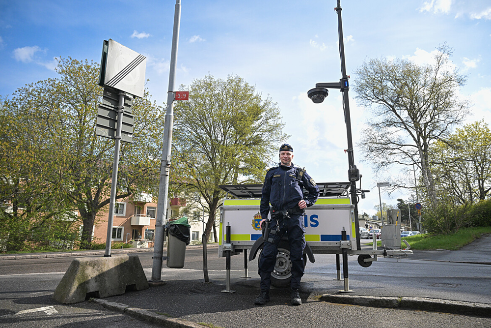 En polis står utomhus vid en rörlig kameravagn som används för kamerabevakning. Det är vår ute.