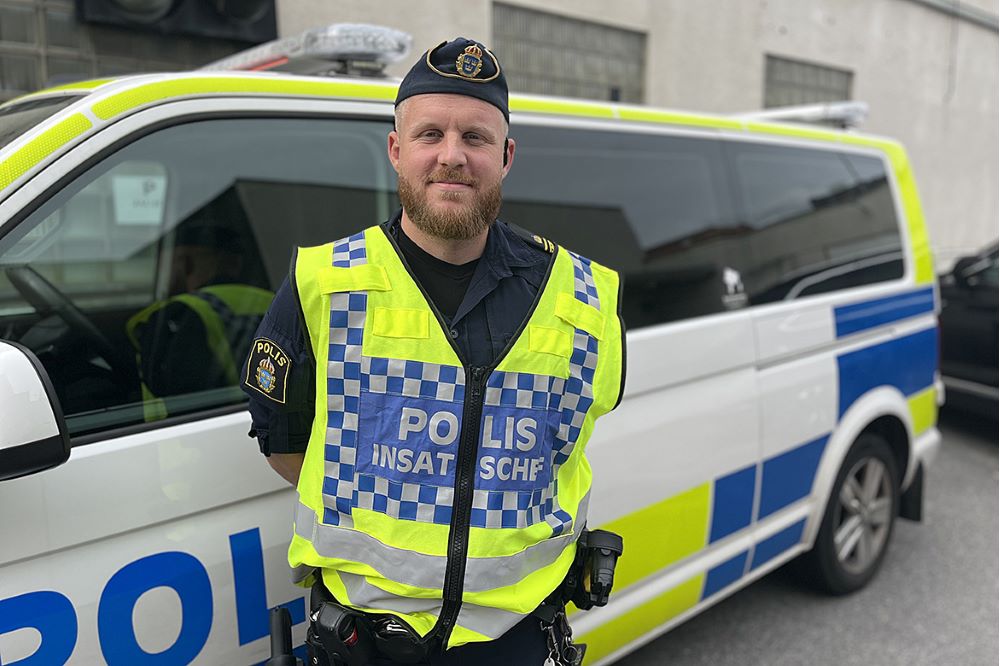 En uniformerad polis, Oscar Berggren, står med reflexväst framför en polisbuss.