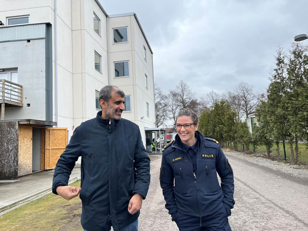 Khalil Assi, ordförande för organisationen WAFK går bredvid kommunpolis Malin Morän. I bakgrunden ses ett vitt bostadshus.