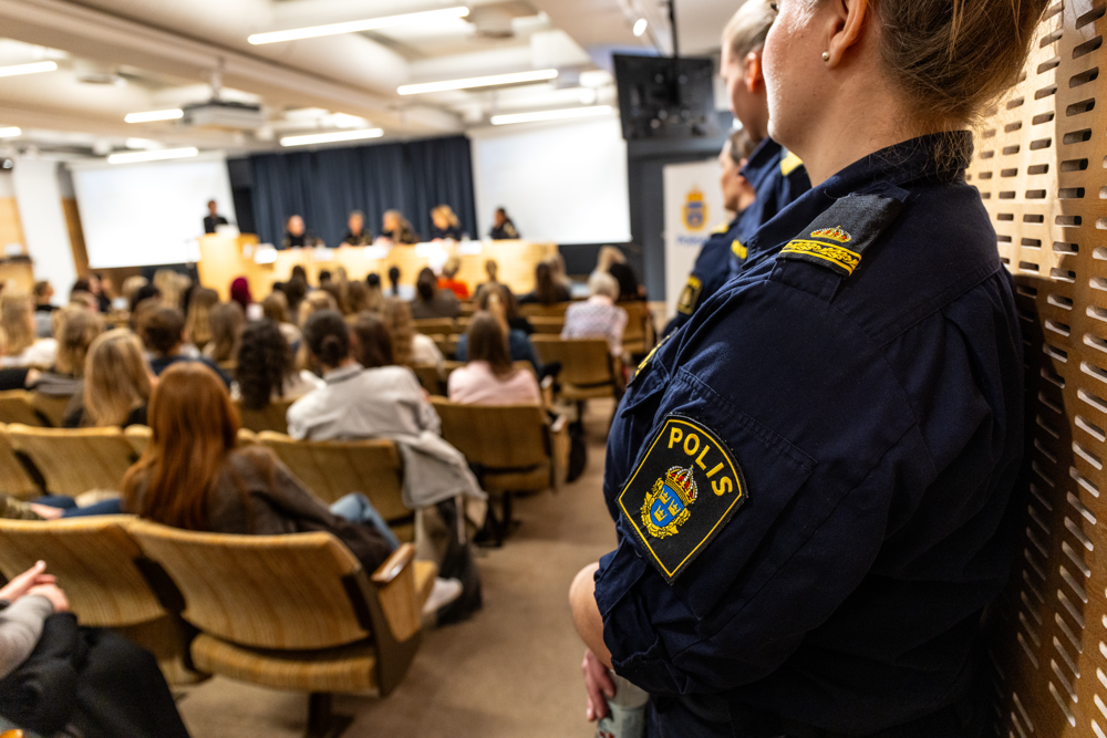 Foto från en tidigare tjejkväll: en polis lyssnar till ett panelsamtal, till vänster syns en publik med kvinnor.