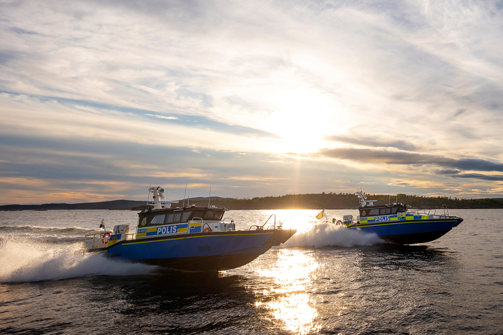Foto på två av polisens båtas som kör snabbt på vattnet med solnedgång i bakgrunden.