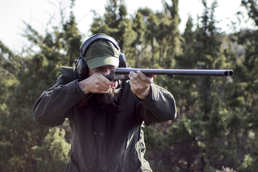 Jäger som står i skogen och siktar med gevär.