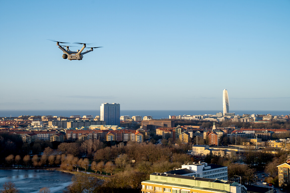 En drönare flyger i luften med delar av centrala Malmö i bakgrunden.