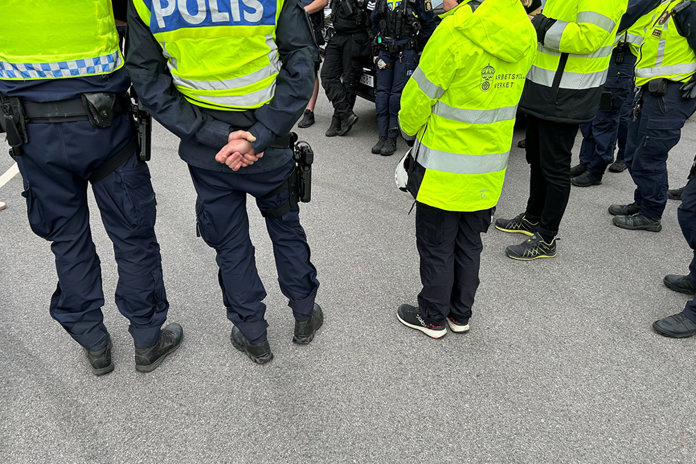 Uniformerad personal från Polismyndigheten och Arbetsmiljöverket står bredvid varandra med ryggarna vända mot kameran. 
