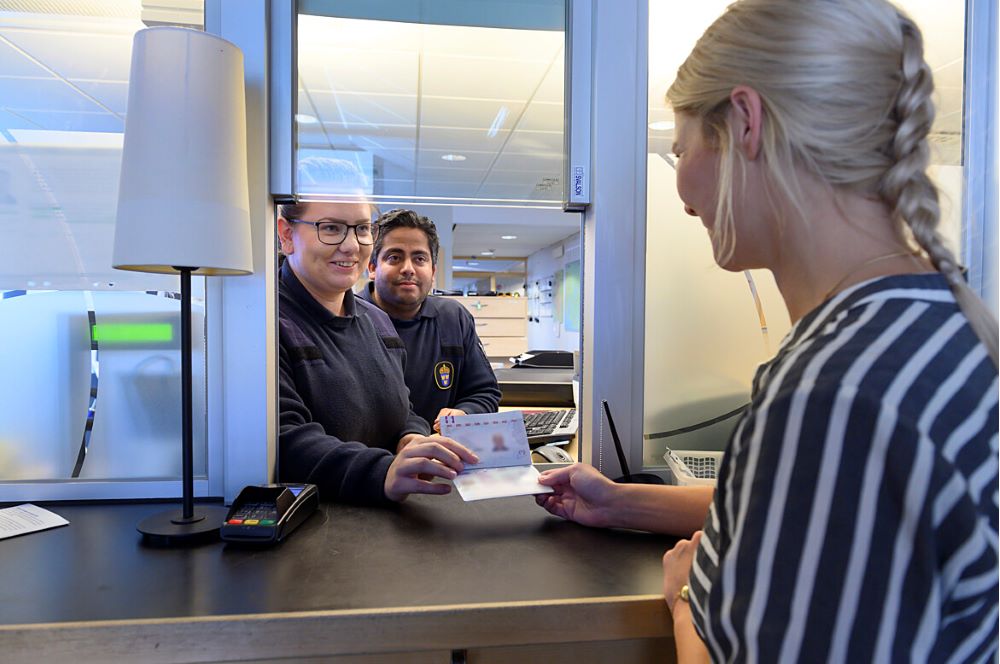 Kvinna som tar emot sitt pass från två passhandläggare i receptionsdisk.