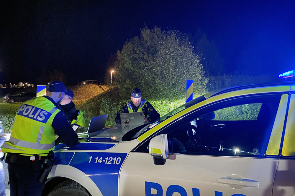 Poliser som står lutade mot polisbil