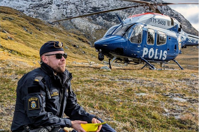 polis på fjället äter en macka med helikopter i bakgrunden .