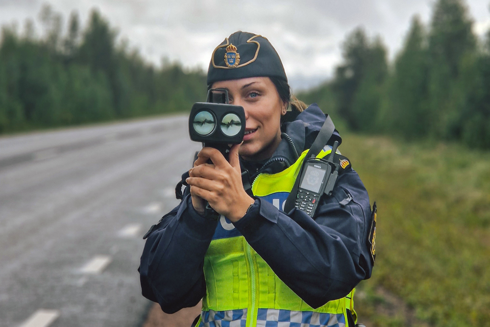 Polis står med hastighetsmätare vid väg.