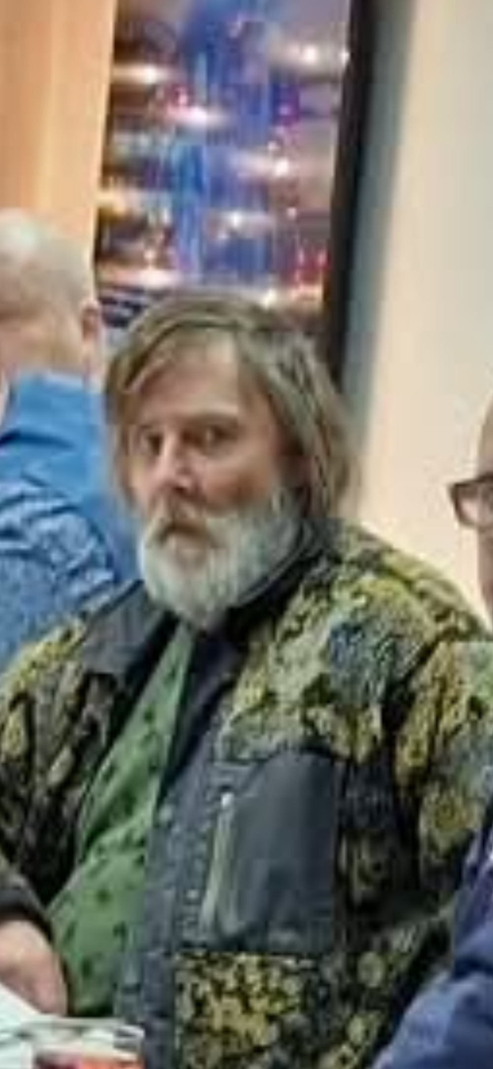 Man med grått hår och grått skägg samt grön kamouflagefärgad jacka.