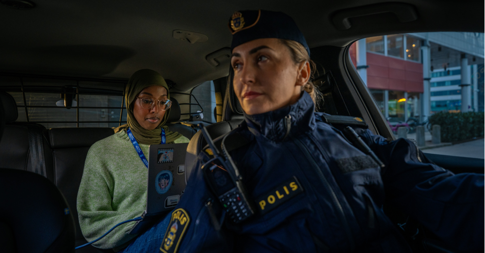 Kvinnlig polis i framsätet på bil, kvinna med dator i knät i baksätet