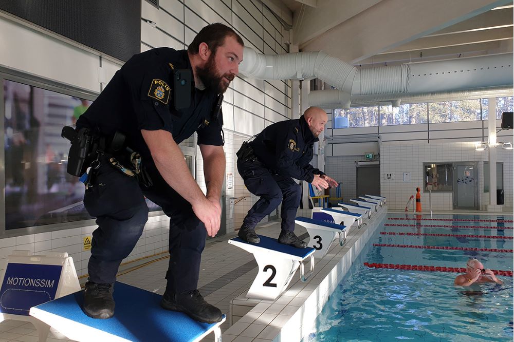 Två poliser i uniform som hjälper till med simträning i en simhall.